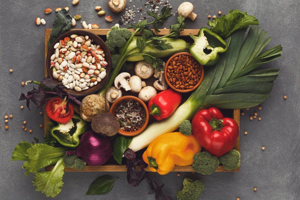 Heap of fresh organic vegetables and greens on wooden tray at black wood background. Healthy natural food. Carrots, pepper, beans and other cooking ingredients top view