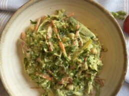 Fresh salad with shredded cabbage, lettuce, carrots, cucumber, bell peppers, chickpeas, and a creamy tofu dressing served in a bowl