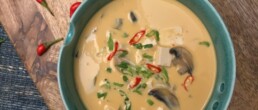 Tofu and Mushroom Coconut Soup in green bowl kept on wooden board
