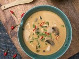 Tofu and Mushroom Coconut Soup in green bowl kept on wooden board