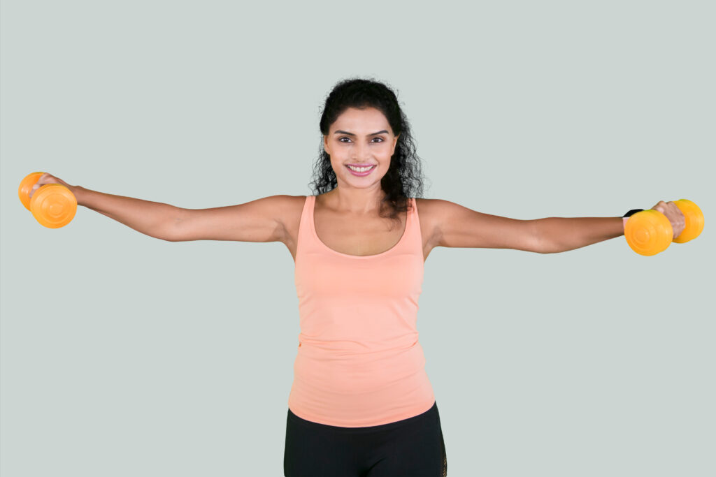 Woman in workout attire holding yellow dumbbells with arms extended sideways, demonstrating a lateral raise exercise.